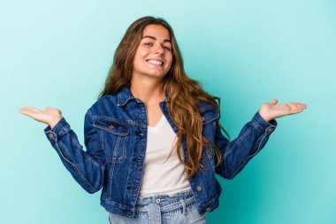 Mavi arka planda izole genç beyaz kadın kollarıyla ölçek yapıyor, mutlu ve kendinden emin hissediyor..