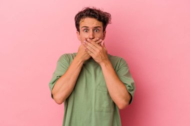 Pembe arka planda izole edilmiş genç beyaz adam elleri endişeli bir şekilde ağzı örtüyor..