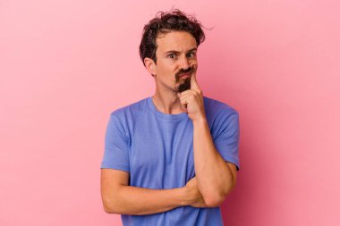 Pembe arka planda izole edilmiş genç beyaz adam alaycı bir ifadeyle kameraya bakıyor..