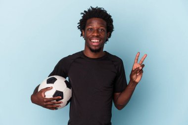 Amerikan futbolu oynayan genç Afrikalı adam mavi arka planda izole edilmiş neşeli ve kaygısız parmaklarıyla barış sembolü gösteriyor..