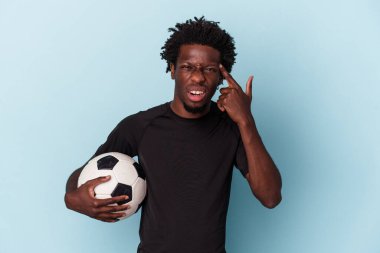 Mavi arka planda izole bir şekilde futbol oynayan genç Afro-Amerikan bir adam işaret parmağıyla hayal kırıklığı jesti yapıyor..