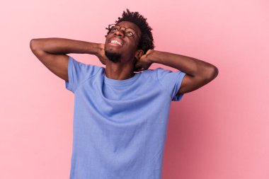 Genç Afrikalı Amerikalı bir adam pembe arka planda izole edilmiş. Kendine güveniyor, elleri başının arkasında..