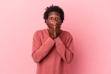 Genç Afrikalı Amerikalı bir adam pembe arka planda izole edilmiş. Şok olmuş, ağzı ellerle kaplanmış, yeni bir şey keşfetmeye hevesli..