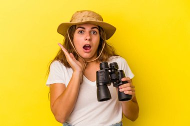 Sarı arka planda dürbün tutan genç beyaz kadın şaşırdı ve şok oldu..