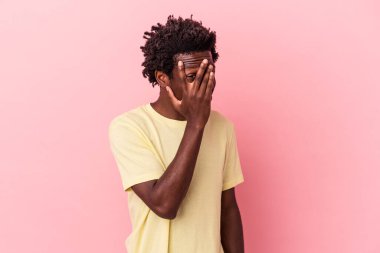 Genç Afro-Amerikalı bir adam pembe arka planda izole edilmiş parmaklarıyla kameraya göz kırpıyor, yüzünü kapatmaktan utanıyor..