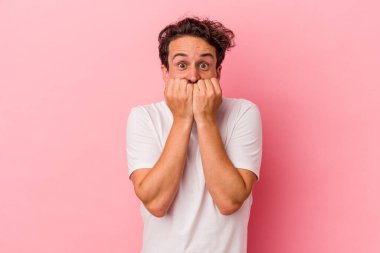 Pembe arka planda izole edilmiş, tırnak yiyen, gergin ve endişeli genç bir beyaz adam..