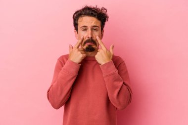 Kafkasyalı genç bir adam pembe arka planda izole edilmiş ağlıyordu, bir şeyden mutsuzdu, acı ve kafa karışıklığı içeriyordu..