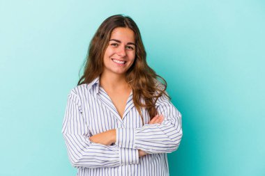 Mavi arka planda izole edilmiş genç beyaz kadın kendini güvende hissediyor, kararlılıkla kollarını kavuşturuyor..