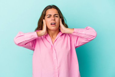 Kafkasyalı genç bir kadın mavi arka planda izole edilmiş kulakları kulaklarıyla kapatıyor çok fazla ses duymamaya çalışıyor..
