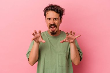 Pembe arka planda izole edilmiş genç beyaz adam pençelerini kedi taklidi yaparken gösteriyor, agresif bir hareket..