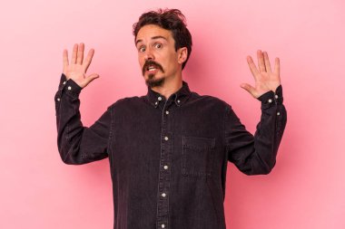 Pembe arka planda izole genç beyaz adam yakın bir tehlike nedeniyle şoka uğruyor.