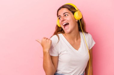 Pembe arka planda müzik dinleyen beyaz bir kadın. Baş parmak uzakta, gülüyor ve kaygısız..