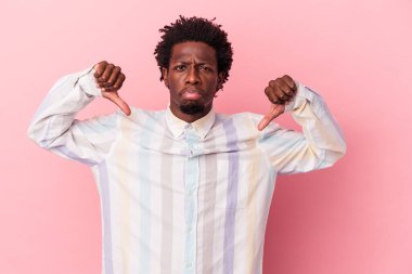 Genç Afro-Amerikalı bir adam pembe arka planda izole edilmiş, hoş olmayan bir jest gösteriyor, başparmakları aşağıda. Anlaşmazlık konsepti.
