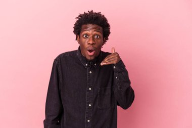 Genç Afrikalı Amerikalı bir adam pembe arka planda izole edilmiş bir şekilde bir şeylere gülüyor, elleriyle ağzını kapatıyor..