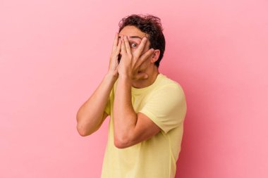 Pembe arka planda izole edilmiş genç beyaz adam parmaklarıyla gözünü kırp korkmuş ve gergin..