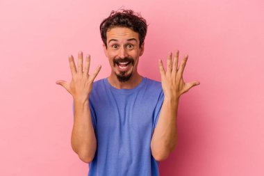 Pembe arka planda izole edilmiş genç beyaz adam on numarayı elleriyle gösteriyor..