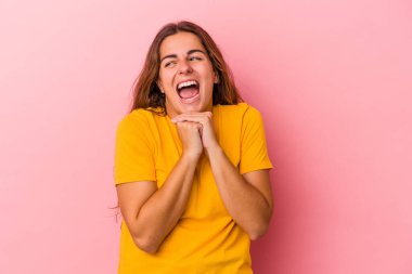 Pembe arka planda izole edilmiş genç beyaz kadın ellerini çenesinin altında tutuyor, mutlu bir şekilde yana bakıyor..