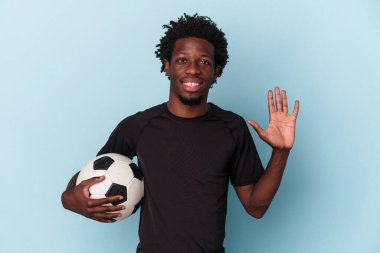 Amerikan futbolu oynayan genç Afro-Amerikalı adam mavi arka planda izole edilmiş, gülümseyen beş numarayı parmaklarıyla gösteriyor..