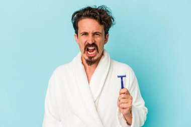 Mavi arka planda izole edilmiş jilet tutan genç beyaz adam çok sinirli ve agresif çığlıklar atıyor..