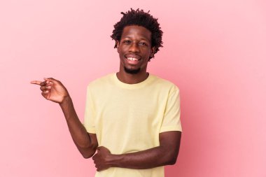 Pembe arka planda izole edilmiş genç Afro-Amerikalı adam mutlu bir şekilde işaret parmağıyla işaret ediyor..