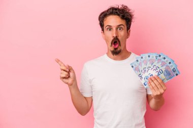 Elinde banknotlar tutan beyaz bir adam var. Pembe arka planda izole edilmiş. Yan tarafı işaret ediyor.