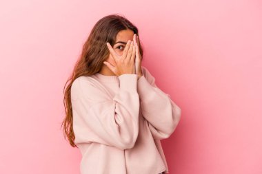 Pembe arka planda izole edilmiş genç beyaz kadın parmaklarıyla gözünü kırp korkmuş ve gergin..