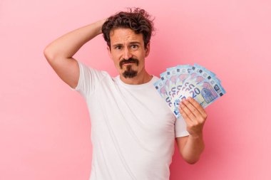 Elinde banknotlar tutan genç beyaz adam pembe arka planda izole edilmiş şoka uğruyor, önemli bir toplantıyı hatırlıyor..