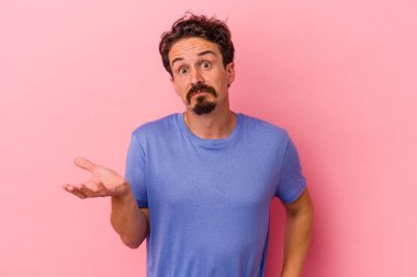 Pembe arka planda soyutlanmış genç beyaz bir adam sorgulama sırasında omuz silkiyor ve şüphe duyuyor..