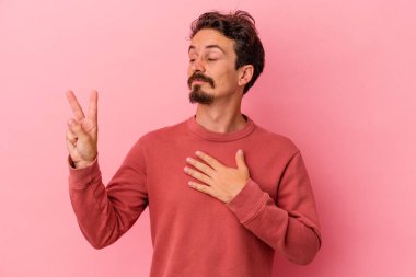 Pembe arka planda izole edilmiş genç beyaz adam yemin ediyor, elini göğsüne koyuyor..