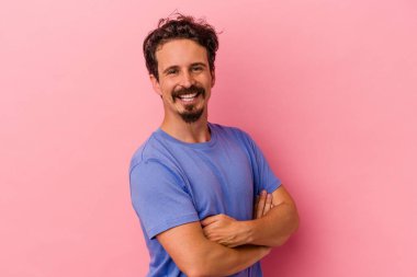 Pembe arka planda izole edilmiş genç beyaz adam kendini güvende hissediyor, kararlılıkla kollarını kavuşturuyor..