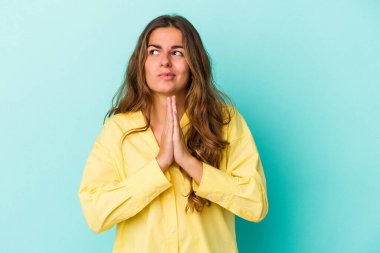 Kafkasyalı genç kadın mavi arka planda izole edilmiş dua ediyor, bağlılık gösteriyor, dindar biri ilahi ilham arıyor..