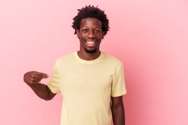 Genç Afro-Amerikalı bir adam pembe arka planda izole edilmiş. Elle bir tişört fotokopisini gösteriyor. Gururlu ve kendinden emin.