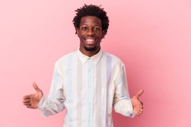 Genç Afrikalı Amerikalı bir adam pembe arka planda izole edilmiş iki eliyle bir şey tutuyor, ürün sunumu..