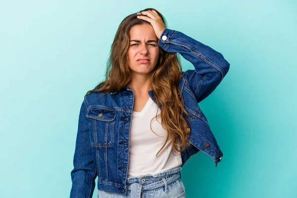 Mavi arka planda izole edilmiş genç beyaz kadın yorgun ve uykulu ellerini başının üstünde tutuyor..