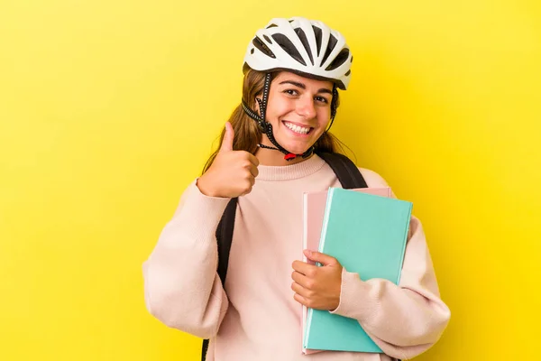 若いですCaucasian学生女性身に着けていますAバイクヘルメット隔離上の黄色の背景笑顔と上げ親指アップ — ストック写真