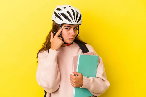 若い白人の学生の女性は 指で寺を指して黄色の背景に隔離された自転車のヘルメットを着て タスクに焦点を当て — ストック写真