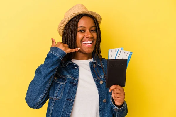 Sarı arka planda pasaportu olan Afro-Amerikalı genç bir kadın cep telefonu hareketini parmaklarıyla gösteriyor..