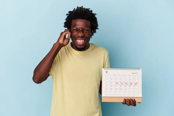 Mladý Africký Američan Drží Kalendář Izolované Modrém Pozadí Zakrývající Uši — Stock fotografie