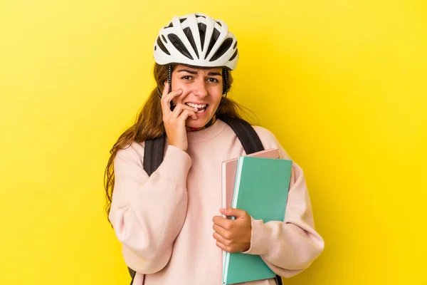 若いです白人学生女性を身に着けています自転車ヘルメット黄色の背景に隔離された指の爪をかむ 神経と非常に不安 — ストック写真