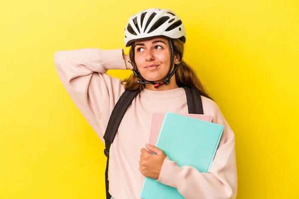 若いです白人学生の女性は 頭の後ろに触れる黄色の背景に隔離された自転車のヘルメットを身に着けています 思考と選択をします — ストック写真