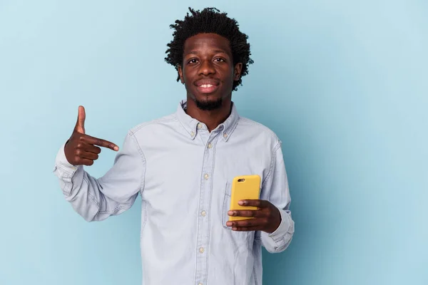 拿着手机的年轻的非洲裔美国人 被蓝色背景的人隔离着 手指着衬衫的复制品空间 自豪而自信 — 图库照片