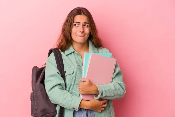 若い白人学生の女性はピンクの背景に孤立した本を持っています混乱しました 疑問と不確定な感じ — ストック写真