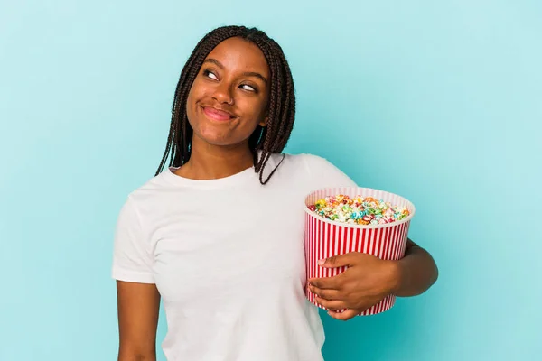 年轻的非洲裔美国女人吃着被蓝色背景隔离的爆米花 梦想着实现自己的目标和目的 — 图库照片