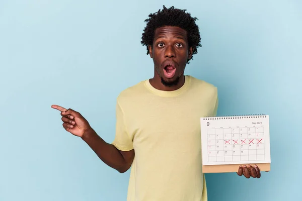 Mladý Africký Američan Drží Kalendář Izolované Modrém Pozadí Ukazuje Stranu — Stock fotografie