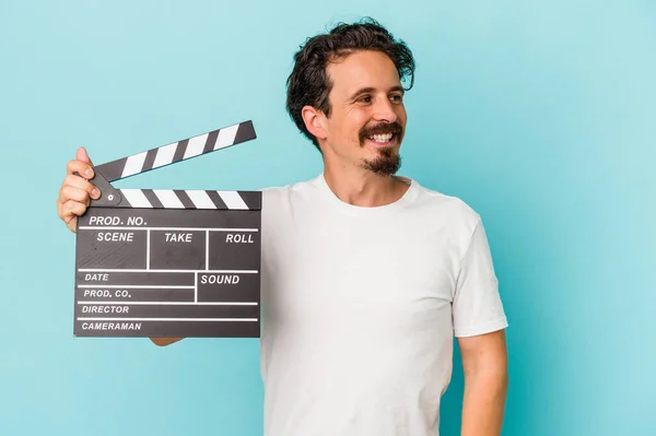 Young Caucasian Man Holding Clapperboard Isolated Blue Background Looks Aside — Stock Photo, Image