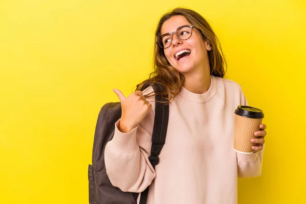 若いですCaucasian学生女性保持コーヒー隔離上の黄色の背景点とともに親指指離れて 笑いと屈託のない — ストック写真