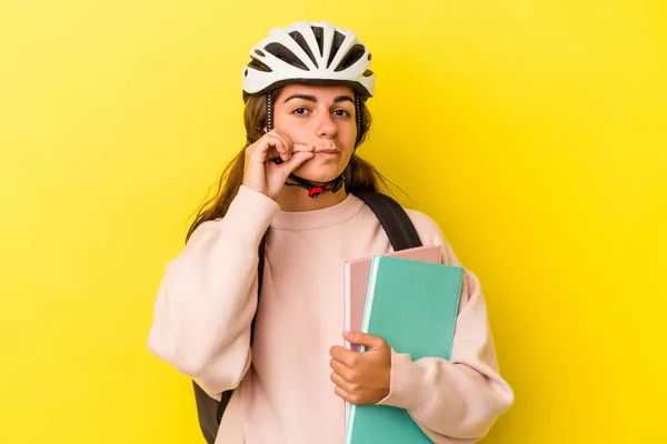 若いですCaucasian学生女性身に着けていますAバイクヘルメット隔離上の黄色の背景とともに指で唇を保ちます秘密 — ストック写真