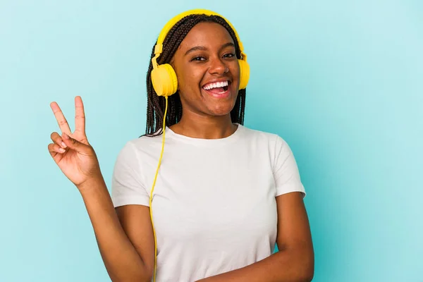 青を基調とした音楽に耳を傾ける若いアフリカ系アメリカ人女性喜びと屈託のない指の平和のシンボルを示す — ストック写真