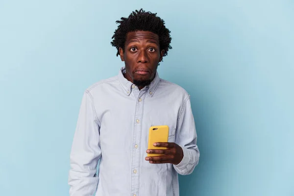 年轻的非洲裔美国人 手持被蓝色背景隔离的手机 耸了耸肩 睁开眼睛迷惑不解 — 图库照片