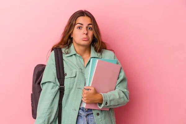 若いですCaucasian学生女性保持本隔離上のピンクの背景Shrugs肩とオープン目混乱 — ストック写真